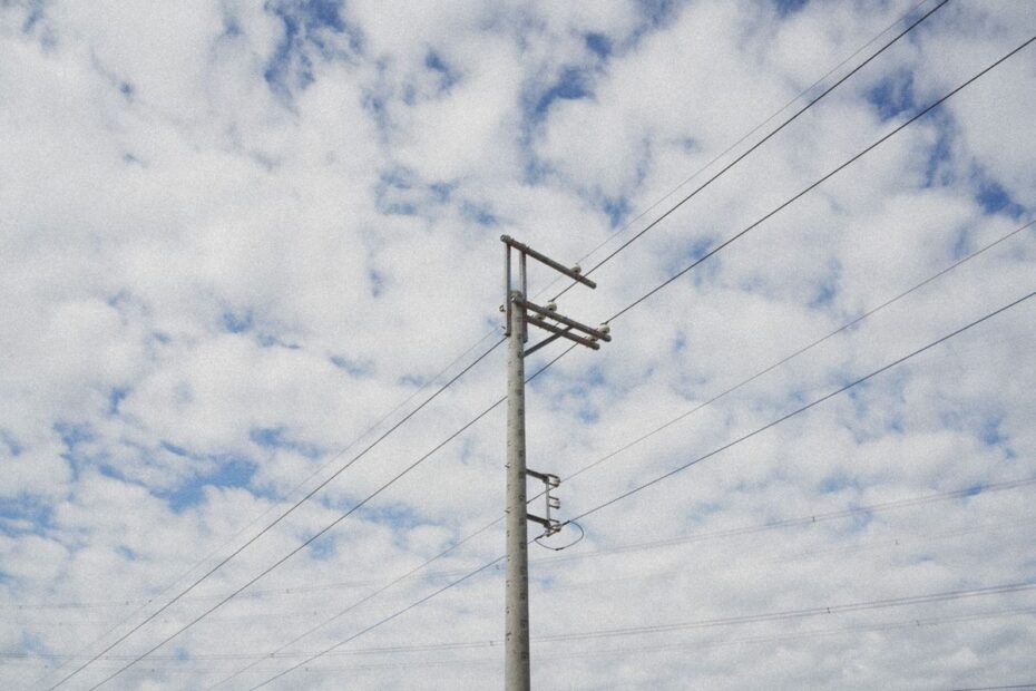 Betonowy słup linii elektroenergetycznej z izolatorami i przewodami na tle zachmurzonego nieba